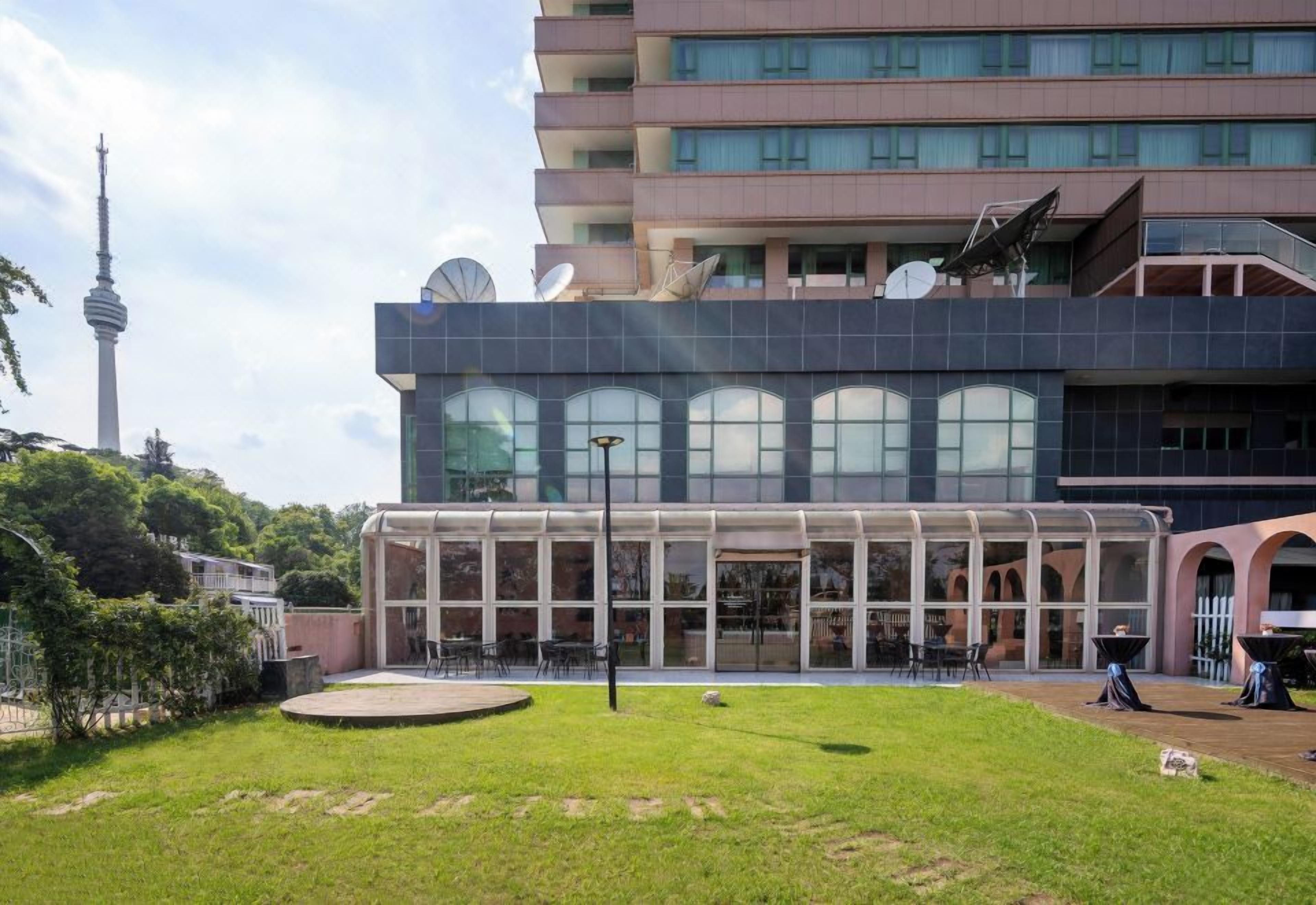 Un bâtiment moderne avec une façade en verre, des antennes paraboliques et une vue sur une tour en arrière-plan.