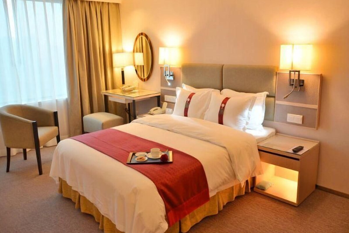A hotel room with a bed, bedside tables, a desk, a chair, and a window with curtains.
