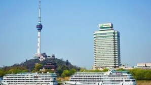 A cruise ship docked near a tall building with a tower, surrounded by greenery. - Holiday Inn WUHAN RIVERSIDE by IHG (Wuhan)