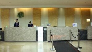 A reception desk with two staff members, a marble counter, and a black carpet leading to the entrance. - Holiday Inn WUHAN RIVERSIDE by IHG (Wuhan)