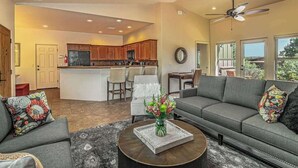 A spacious living room with a gray sofa, a coffee table, and a dining area with a chandelier. - Myrinn – Private Hot Tub & Red Rock Views (Sedona)