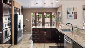 Una cocina moderna con electrodomésticos de acero inoxidable, armarios de madera oscura, encimeras de granito e iluminación colgante.