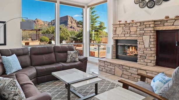 Una sala de estar moderna con chimenea de piedra, sofá de cuero y grandes ventanales con vistas a las montañas.