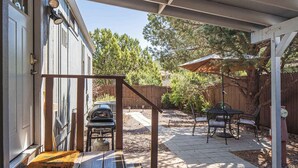 Ein überdachter Patio-Bereich mit Grill, Sitzgelegenheiten im Freien und einer Holzterrasse, die zu einem Haus führt.