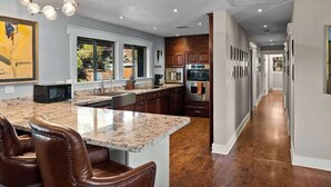 Una cocina moderna con encimeras de granito, electrodomésticos de acero inoxidable y una isla central con taburetes de bar.