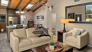A spacious living room with a sofa, armchair, and coffee table, a dining area with a table and chairs, and a kitchen with modern appliances.