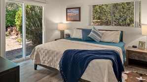 A bedroom with a bed, a nightstand, a lamp, and a view of the outdoors.