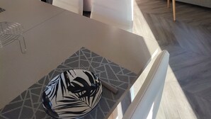 Moderni olohuone, jossa on beigenvärinen sohva, valkoinen sohvapöytä ja ruokailutila, jossa on pöytä ja tuolit. Ikkunasta avautuu näkymä kaupunkiin.