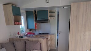A modern living room with a sofa, a small round table, and a kitchen area with wooden cabinets and a gas stove. - 8-person mobile home, ideal for families! Sheets & towels included (Condrieu)
