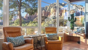 A room with large windows offering a view of red rock formations and trees. There are two leather chairs with patterned cushions.