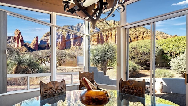 A dining area with a glass table and chairs, a decorative vase, and a view of red rock formations through large windows.
