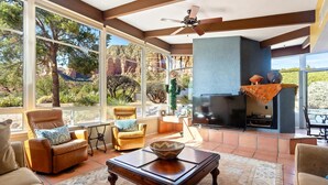 A spacious living room with large windows, a ceiling fan, and a fireplace.