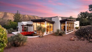 A modern house with a patio, large windows, and a view of the surrounding landscape.