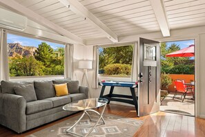A living room with a sofa, a glass coffee table, a foosball table, and a view of the outdoors. - Myrinn–Red Rock Views & Hot Tub Near Uptown Trails (Sedona)