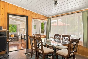 A dining area with a glass table and wooden chairs, a television, and a sofa in the background. - Myrinn–Red Rock Views & Hot Tub Near Uptown Trails (Sedona)