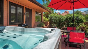 Un bain à remous avec un espace patio comprenant une table et des chaises, ainsi qu’un parasol rouge.