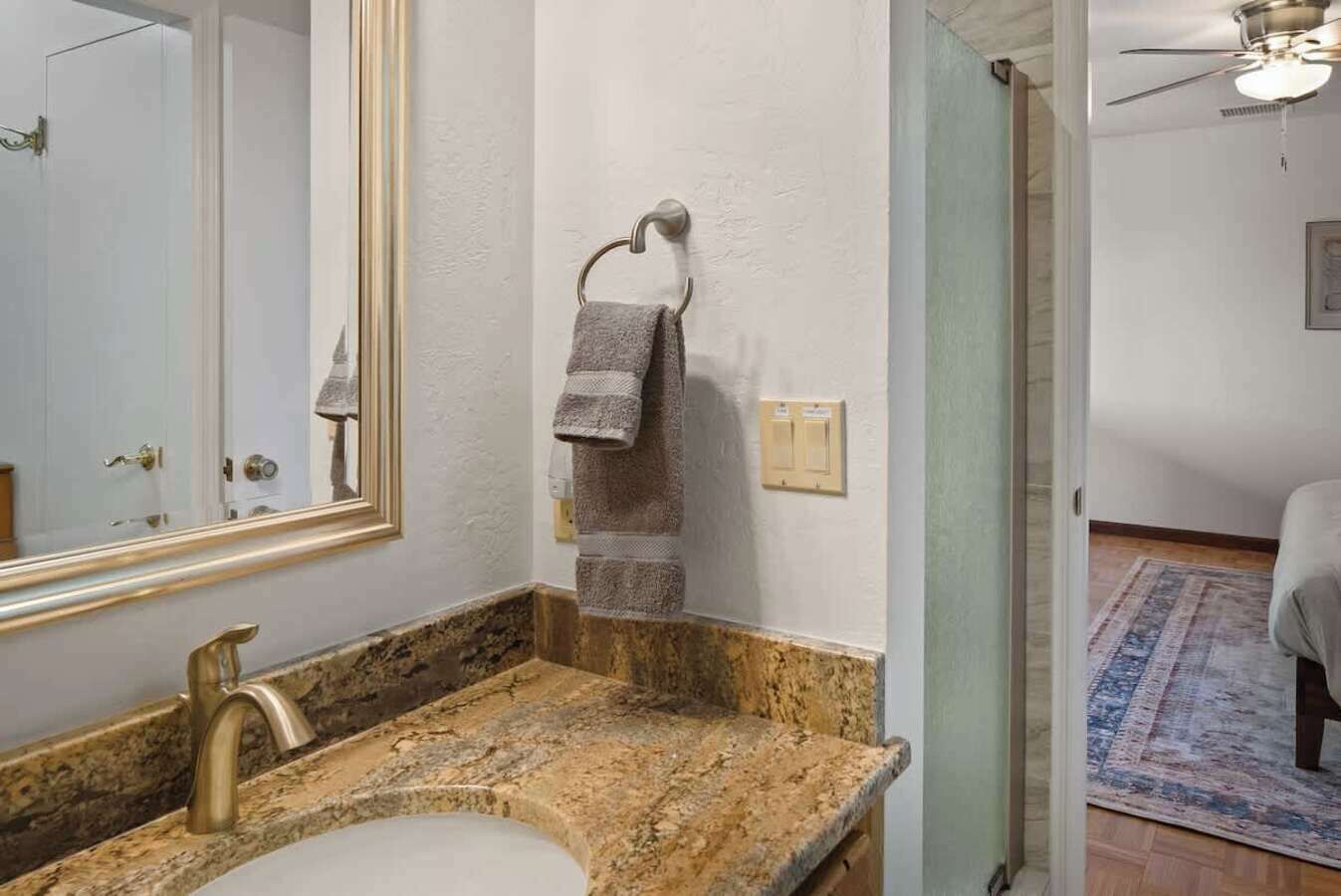 Une salle de bain avec un lavabo doté d’un plan de travail en granit, un grand miroir et une serviette suspendue à un porte-serviettes.