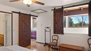 Una habitación con una cama, un banco de madera, una silla, un armario y una ventana con vistas a árboles.