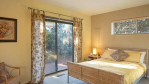 Ein Schlafzimmer mit einem Korbmöbelbett, einem Sessel, einem Nachttisch mit Lampe und einem Fenster mit Jalousien.