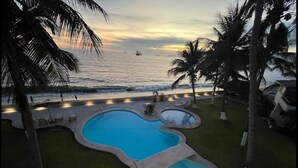 A swimming pool with a curved design, surrounded by palm trees and a view of the ocean at sunset. - OCEAN VIEW PENTHOUSE WITH TERRACE (Manzanillo)