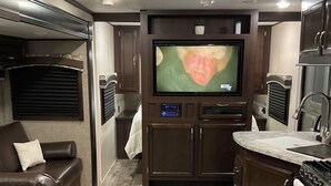 Un intérieur de camping-car compact comprenant un espace de vie, un coin cuisine et un téléviseur fixé au mur.