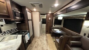 Un intérieur de camping-car compact comprenant un coin cuisine, un espace repas et des sièges.