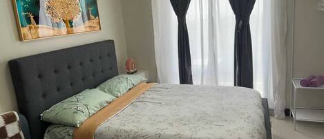 Un dormitorio con cama, mesita de noche, aire acondicionado de pared, un cuadro y ventana con cortinas.