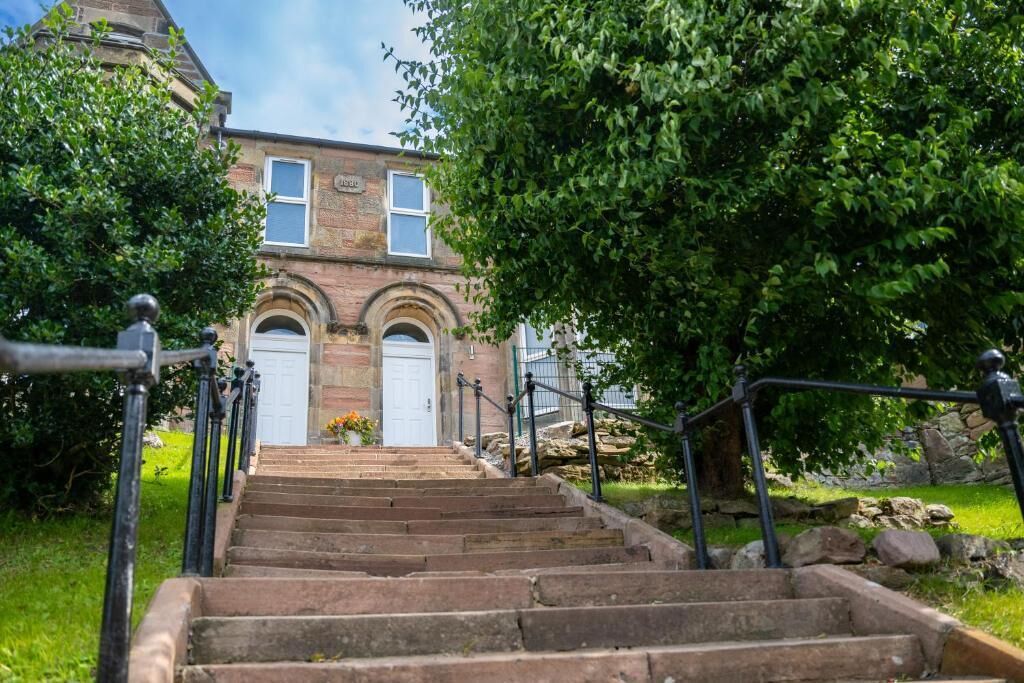 A set of stone steps leading to a building with arched windows and a white door.