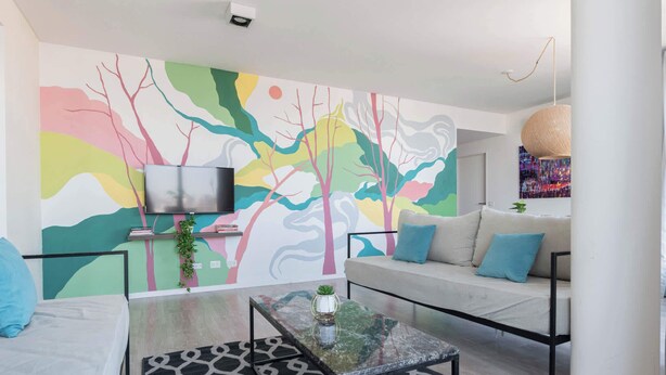 A modern living room with a colorful mural, a sofa, a coffee table, and a TV. - MOT Rentals + GuateFlat 'G' 2 Bd in Palermo Soho (Buenos Aires)