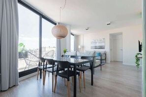 A modern living room with a dining area, large windows, and a view of the city.