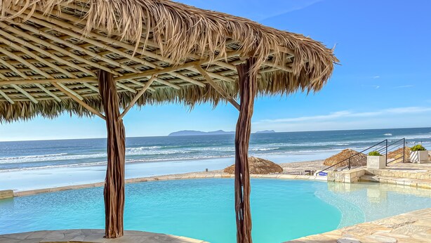 Un área de piscina con techo de paja, suelo de piedra y vistas al océano.