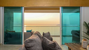 Un salón moderno con un sofá, una mesa de centro y vistas al mar a través de puertas de cristal.