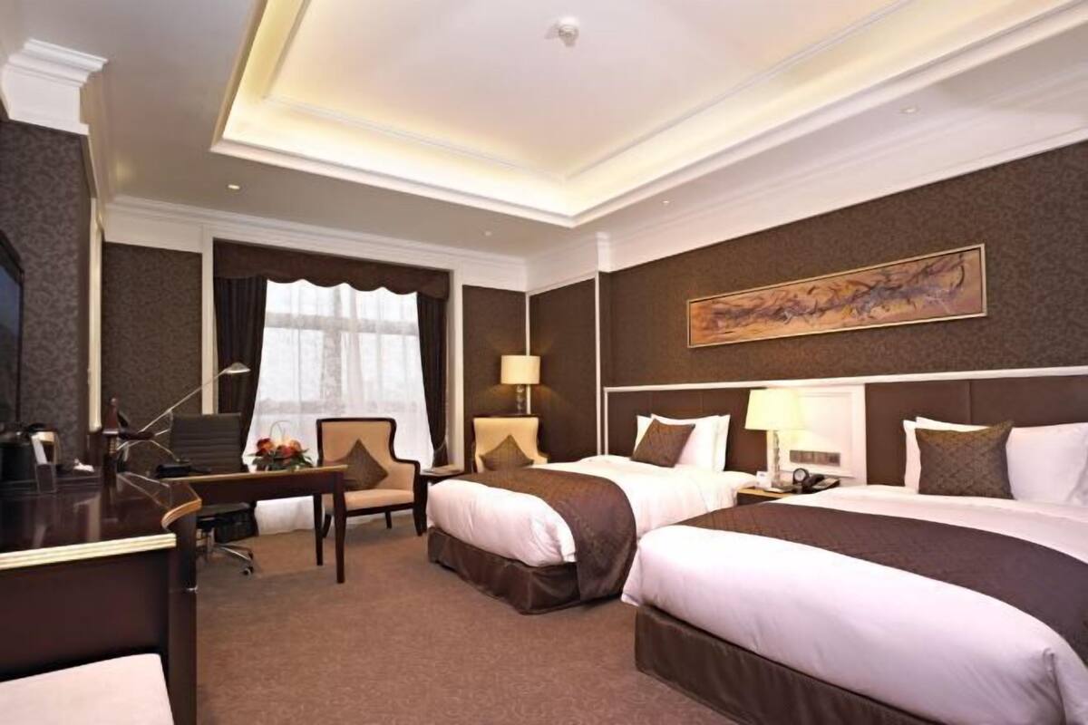 A hotel room with two beds, a desk, a chair, and a large painting on the wall.
