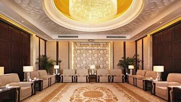 A formal meeting room with a large chandelier, sofas arranged in a semi-circle, and a patterned carpet.
