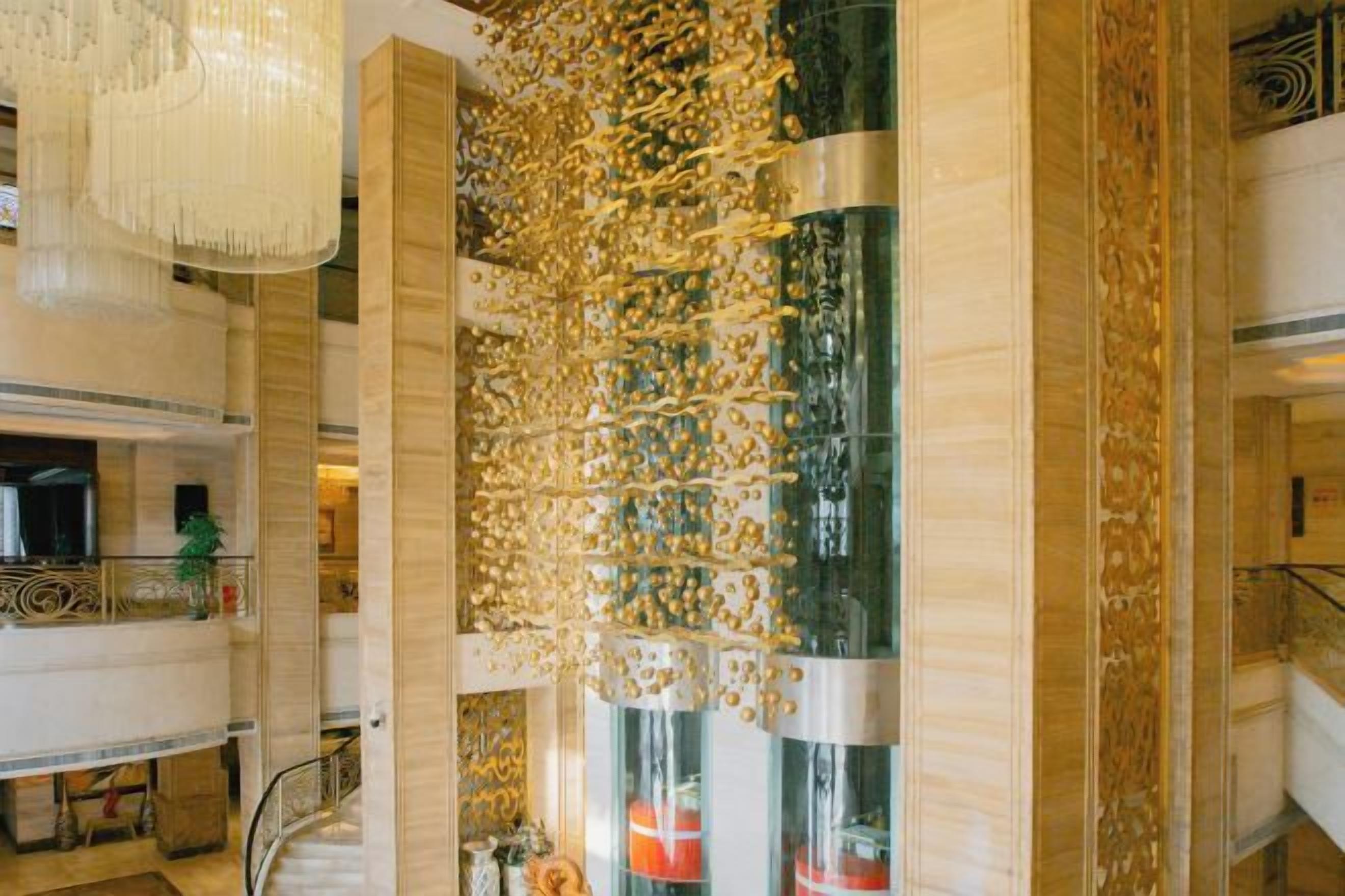 Um saguão com uma escadaria imponente, uma parede decorativa com elementos suspensos e um candelabro.