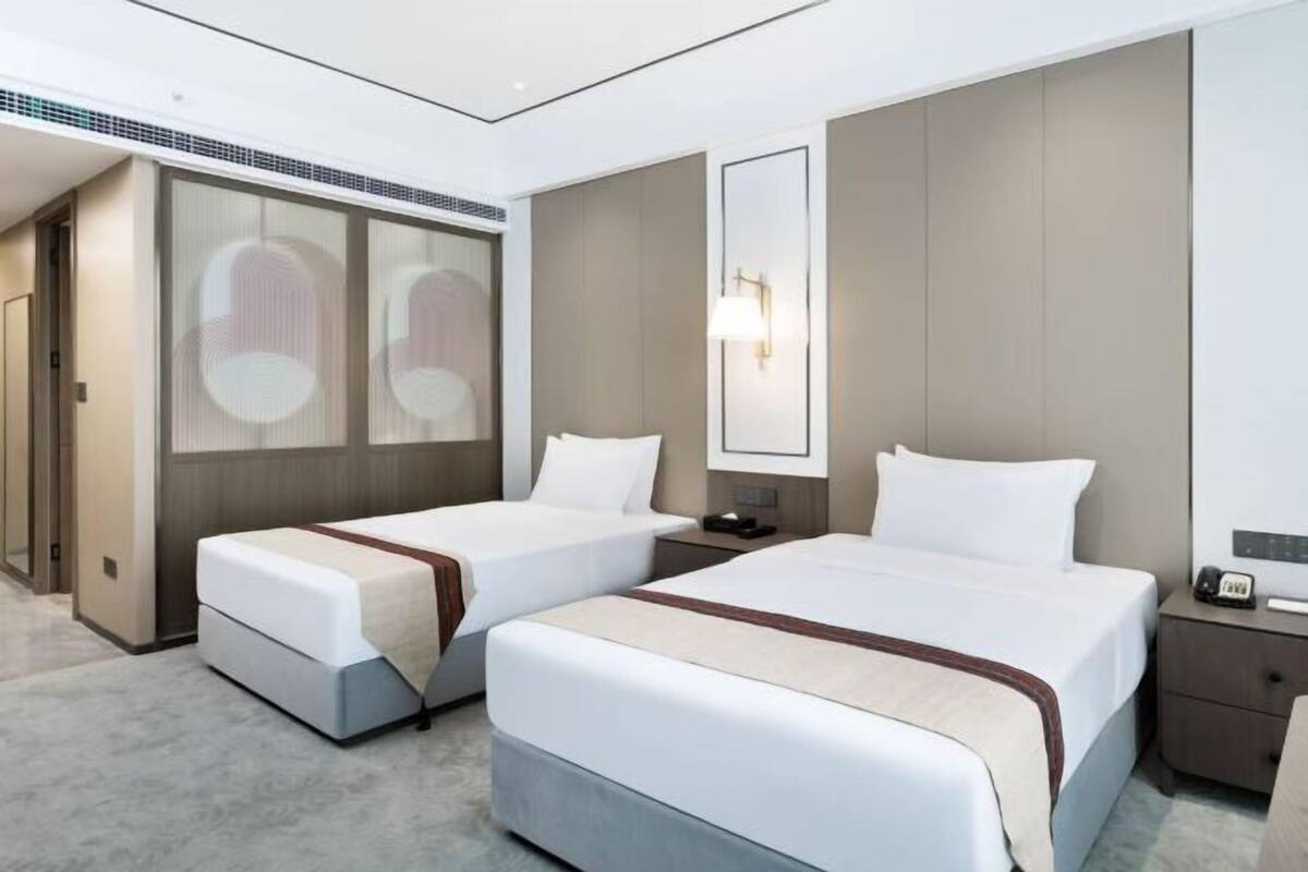 A hotel room with two beds, a large mirror, a nightstand, and a wall-mounted lamp.