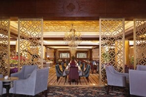 A hotel lobby with a chandelier, a dining area with tables and chairs, and decorative wooden panels. - Rui'er Hotel (Chongqing)