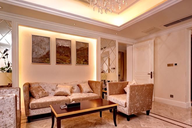 Uma sala de estar com sofá, poltrona e mesa de centro, um candelabro e quadros na parede.