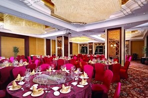 A banquet hall with round tables set for dining, red chairs, and a carpeted floor.
