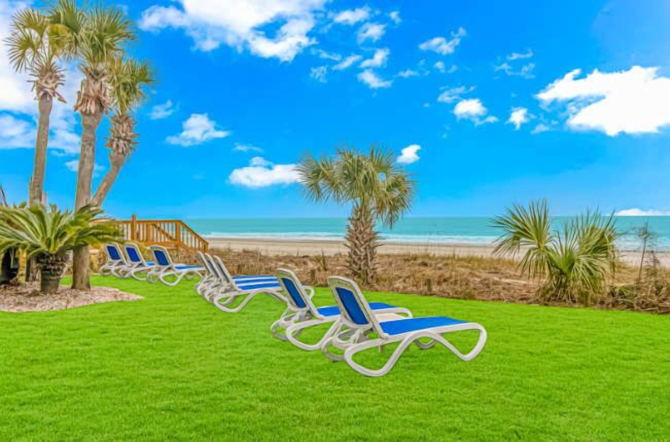 A beachside resort with a row of sun loungers, palm trees, and a wooden deck.