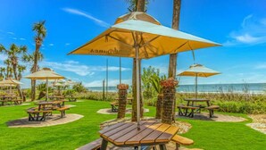 Espace extérieur aménagé avec des parasols, une pelouse et une vue sur la plage.