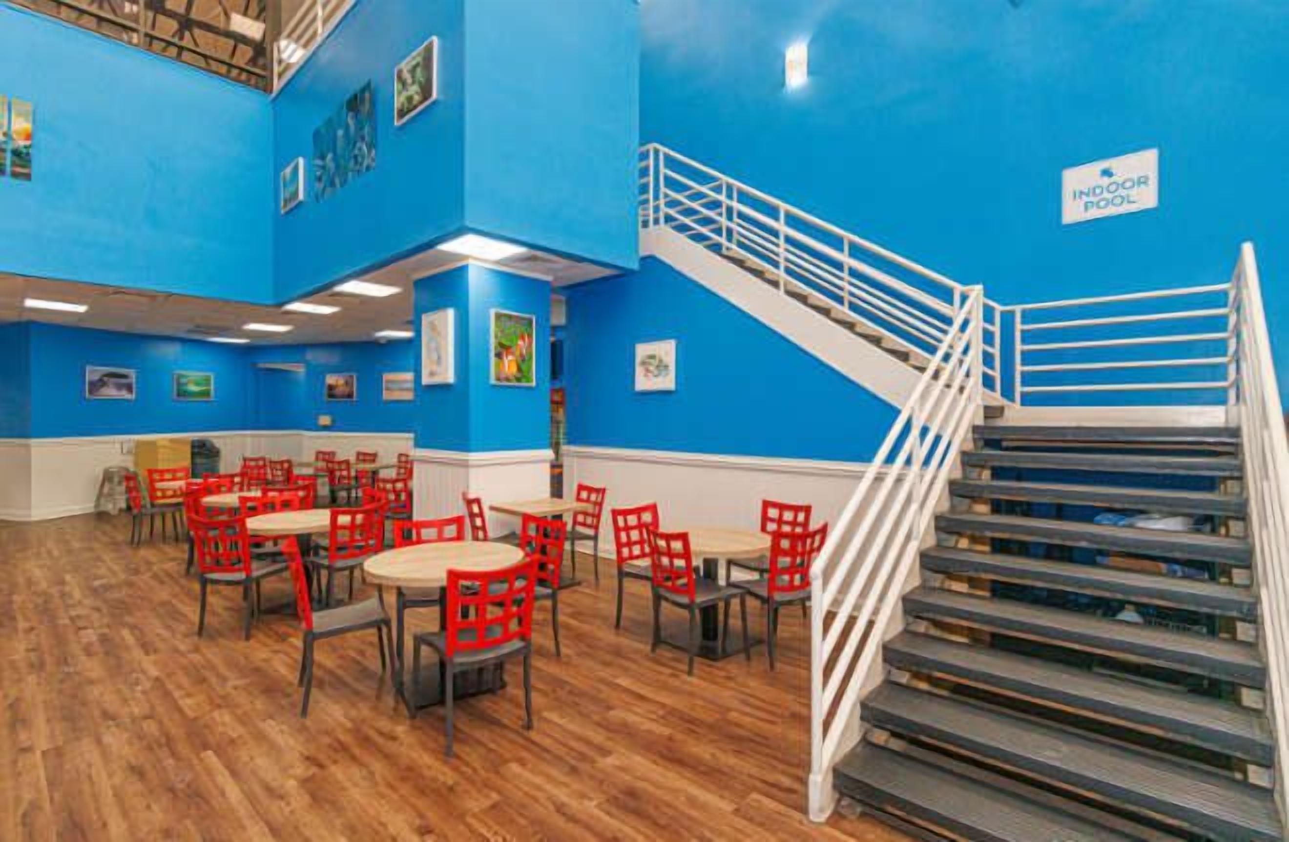 A dining area with red chairs and tables, a staircase, and a blue wall with a sign.