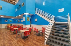Un espace repas avec des chaises et des tables rouges, un escalier et un mur bleu orné d’une enseigne.