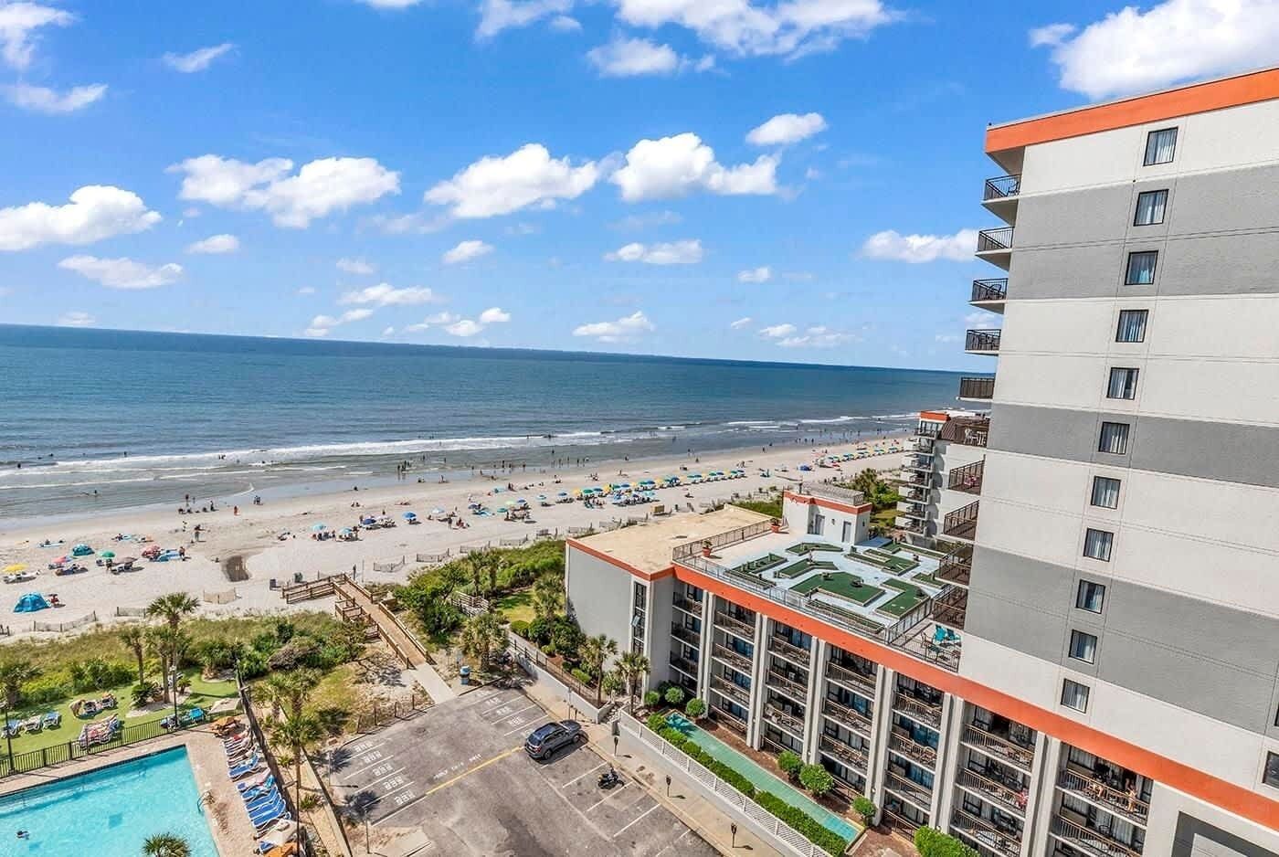 A hotel with a rooftop pool, a beach view, and a parking area.