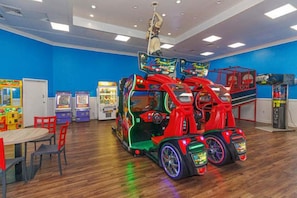 Une salle avec des jeux d’arcade, un espace de jeux sur le thème des voitures rouges et une table avec des chaises.