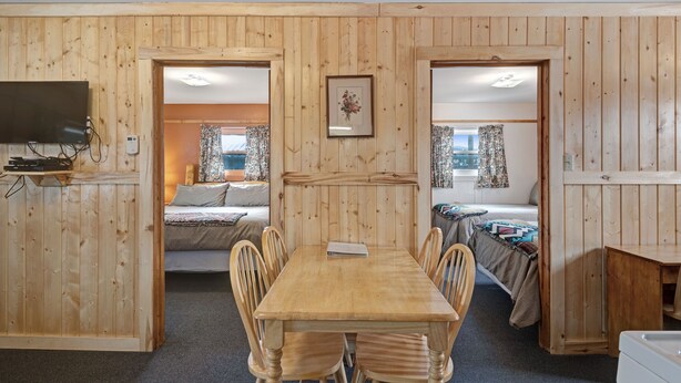Een kamer met houten lambrisering, een eettafel met stoelen, een televisie en twee bedden met gordijnen.