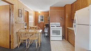 Een compacte keuken met houten kastjes, een witte kookplaat en een eethoek met een tafel en stoelen.