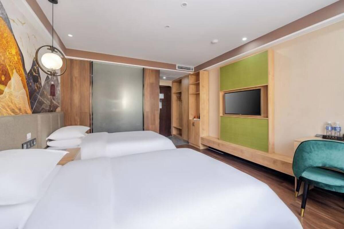 Une chambre d’hôtel avec deux lits, une télévision, un bureau avec une chaise et un tableau au mur.