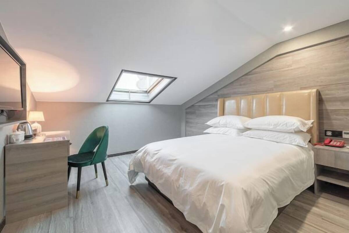 Une chambre avec un puits de lumière, un lit avec une literie blanche, un bureau avec une lampe et une chaise.