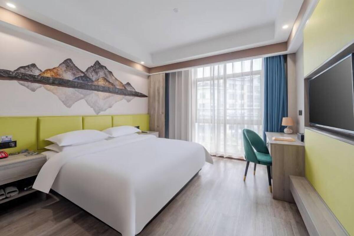 Une chambre d’hôtel équipée d’un lit, d’un bureau, d’une chaise, d’une télévision et d’une fenêtre avec des rideaux.